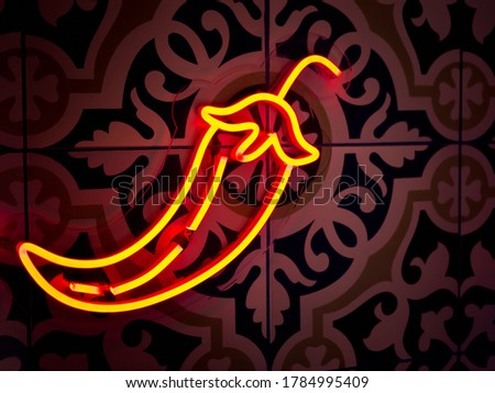 Hot chilli shaped neon sign in bright orange colours glow in the dark on pattern tiles wall background.
