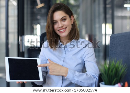 Young happy business woman showing blank tablet computer screen in office.