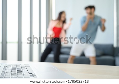Laptop notebook computer on the table with happy and relax young couple lover wearing casual dress together dancing in living room at home. Positive relationship concept.