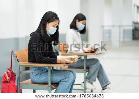 Female teenager college students wears face mask and keep distance while studying in classroom and college campus to prevent COVID-19 pandemic. Education stock photo.
