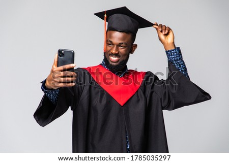 Young african man graduate in gown and cap take selfie over white background