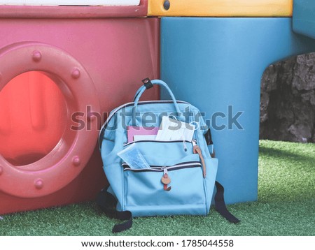 COVID-19 prevention , back  to school  and new normal  concept.School backpack with  sanitizer gel and  surgical mask with playground equipment on green grass.