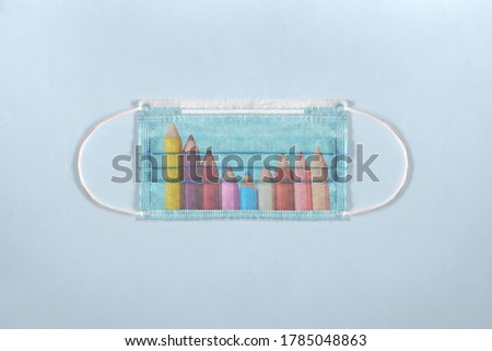 A worn-out surgical mask for children with the drawing of some colored pencils on the front on a blue background fabric texture. Back to school concept.