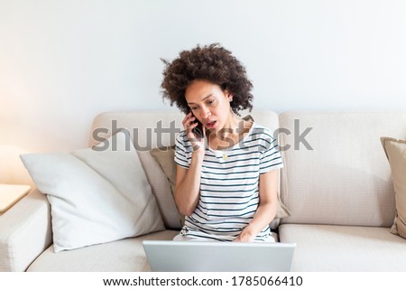 Woman sitting on sofa with laptop and talking on phone at home. Young successful businesswoman working from home while talking at phone. College student studying on laptop and using phone.
