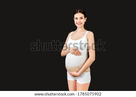 Portrait of pregnancy bandage dressed on pregnant woman for reducing backpain at black background with copy space. Orthopedic abdominal support belt concept.