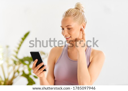 fitness, technology and healthy lifestyle concept - happy smiling young woman with smartphone and earphones at home or yoga studio