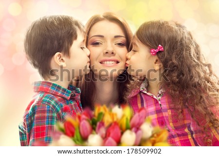 Portrait of children kissing her mother with flowers. Mother`s day concept. Family holiday