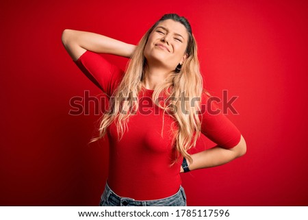 Young beautiful blonde woman wearing casual t-shirt standing over isolated red background Suffering of neck ache injury, touching neck with hand, muscular pain