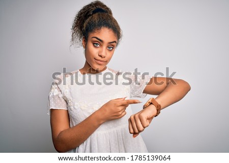 Young beautiful african american girl wearing casual t-shirt standing over white background In hurry pointing to watch time, impatience, upset and angry for deadline delay Royalty-Free Stock Photo #1785139064