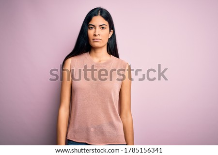 Young beautiful hispanic fashion woman wearing casual sweater over pink background with serious expression on face. Simple and natural looking at the camera. Royalty-Free Stock Photo #1785156341