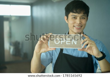close up front of young business owner man holding open sign board to promote and inform reopening at cafe after lock down due to coronavirus pandemic for business and startup concept