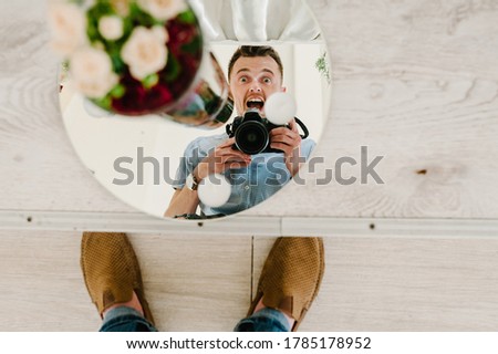 A man takes a picture of himself in the mirror on the camera. The guy takes a selfie photo. Grooming, technology and people concept.
