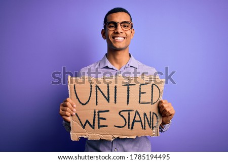 African american activist man asking for union holding banner with united stand message with a happy face standing and smiling with a confident smile showing teeth