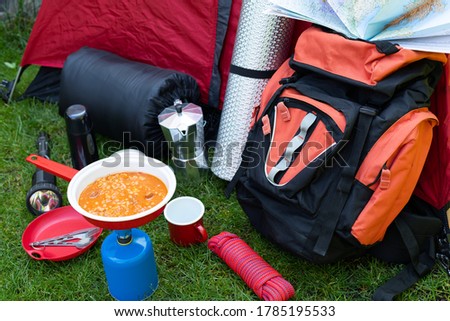 Picture of camping tools on the grass - backpack, tent, gas tank, cans, compass, etc - ready to go in the woods 