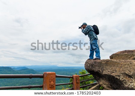 A photographer standing on a hilltop at sunrise at Pha Mo Daeng, Si Sa Ket Province, Thailand, ASIA.