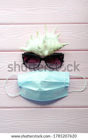 Sea shells, sunglasses and protective mask on a pink wooden background. Summer 2020 and vacation against coronavirus and other infections. Travel creative concept. Copy space, flat lay. Vertical photo