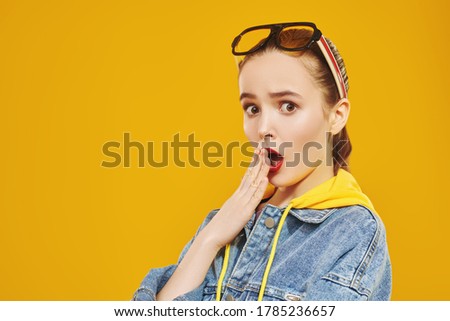 Modern youth look. Emotional pretty young girl in bright summer jacket is posing on a yellow background with modern sunglasses. Beauty, fashion.