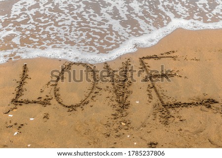 The inscription "love" on the sea sand with the incoming wave. Sandy beach with waves.