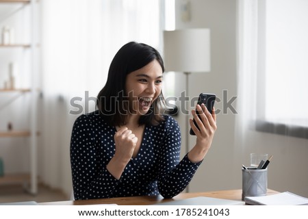 Excited Vietnamese young woman look at cellphone screen triumph win online lottery or app game. Overjoyed Asian millennial girl feel euphoric read good news email on smartphone. Success concept Royalty-Free Stock Photo #1785241043