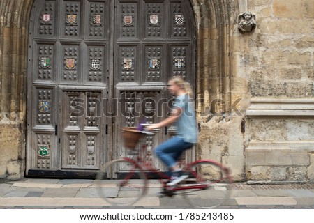 Female Student Riding Old Fashioned Bicycle Around Oxford University College Buildings With Motion Blur