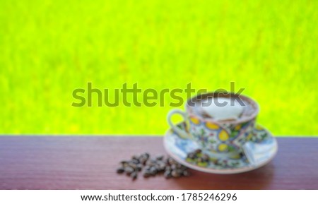 The picture of blur cappuccino coffee cup and coffee beans with blurred rice field rural in the morning  light, Relaxation concept.