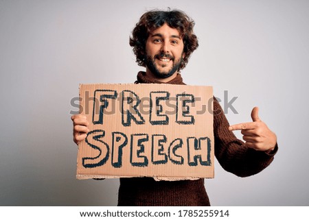 Young handsome man with beard asking for rights holding banner with free speech message very happy pointing with hand and finger