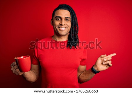 Young african american afro man drinking cup of coffe over red background very happy pointing with hand and finger to the side