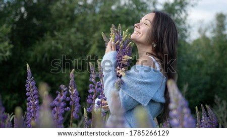 Young pretty woman with a bouquet among flowers violet lupins