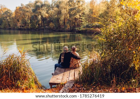 Senior family couple relaxing by autumn lake. Man and woman enjoying nature and hugging sitting on pier Royalty-Free Stock Photo #1785276419