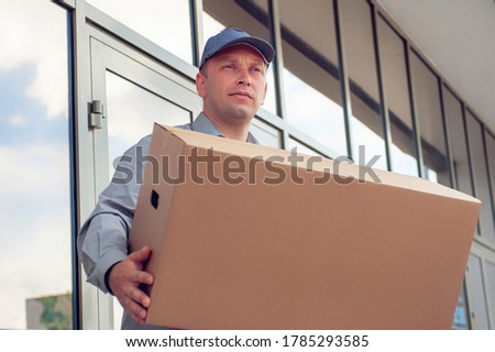 A man in a gray suit in his hands with a cardboard box against the background of the supermarket. Concept on the topic of postal delivery