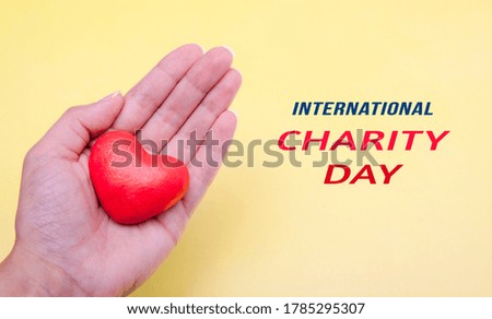 Red heart in hand on a yellow background with text International Charity Day