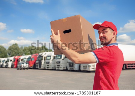 A man in a red suit in his hands with a cardboard box against the background of the van. Concept on the topic of postal delivery