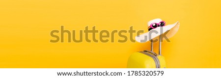 sun hat and sunglasses on suitcase handle on yellow background, panoramic shot