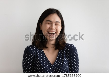 Close up of overjoyed millennial Asian female isolated on grey studio background laugh at funny joke. Happy young Vietnamese woman have fun smile, show healthy white teeth. Humor, entertainment