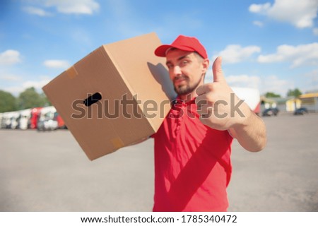 A man in a red suit in his hands with a cardboard box against the background of the van. Concept on the topic of postal delivery