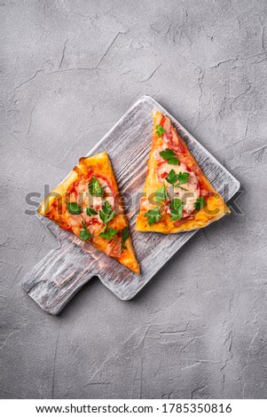 Hot pizza slices with mozzarella cheese, ham, tomato and parsley on wooden cutting board, stone concrete background, top view