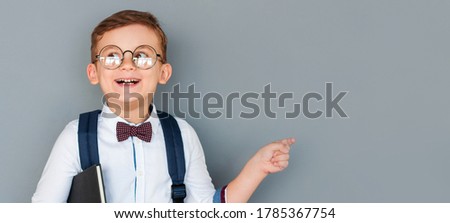 Cheerful, mischievous boy holds a book in his hands, standing at the blackboard. an excited child on a grey background directs its attention to the free space. Back to school.