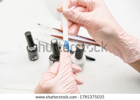 Manicurist at work in the office. Drawing gel polish on tips, creating a picture. Equipment and inventory of a manicure cabinet