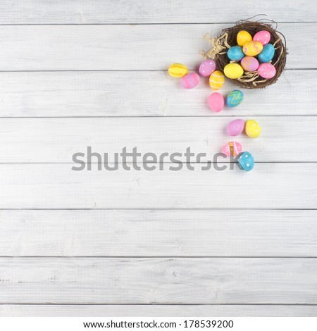 Colorful Easter Egg Nest Overflowing from Up Above with Extra White or Gray Wood Board Background for room or space for copy, text, words.  A flat lay with square crop