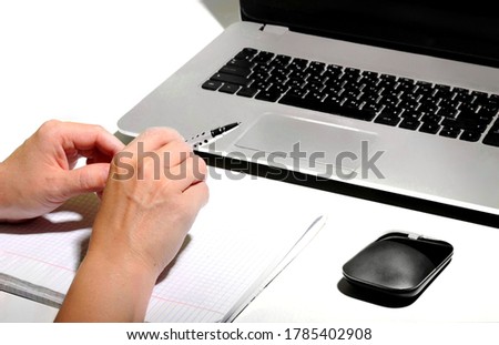 A man sits and works at a white office table on which there is a computer with a keyboard sheet of paper pen PC mouse