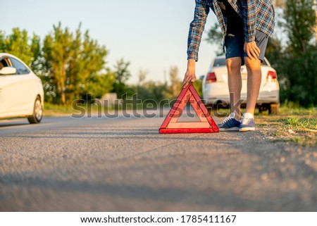 young man holding a red triangle and put it on the road, the sign of car accident