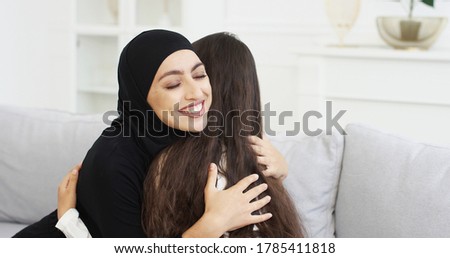 Beautiful young mother in hijab talking with little teen daughter. Muslim woman in headscarf having talk with little girl on couch at home and hugging. Mom's love hugs. Rear. Back view. Royalty-Free Stock Photo #1785411818