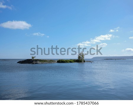 View of a rocky island with two isolated trees in a lake in Sweden. It is a clean image with calm waters and a blue sky background with a few clouds. The photograph is shot with a medium format camera