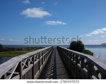 View of a wooden walkway leading to a small island. It is a perspective shot. There is a blue sky with som clouds. It is shot with a medium format camera.