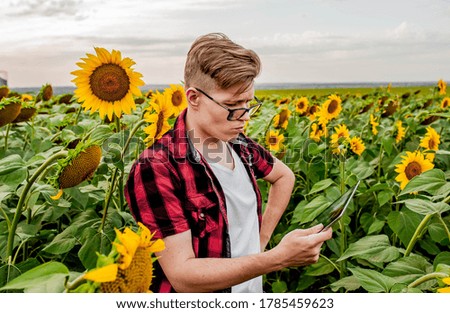 
The guy is holding a tablet in a field with sunflowers. Agriculture manager concept