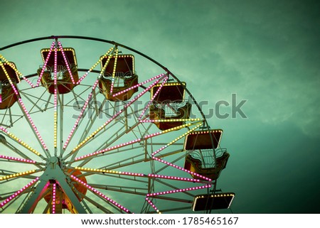 Colorful ferris wheel at dusk, illuminated by neon lights. Background with copy space. Toned green image. Rosolina Mare amusement park, Veneto, Italy.