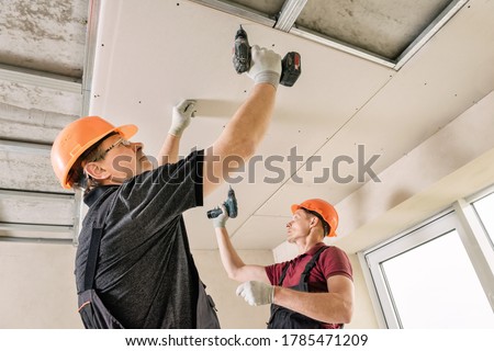 Installation of drywall. Workers are using screws and a screwdriver to attach plasterboard to the ceiling. Royalty-Free Stock Photo #1785471209