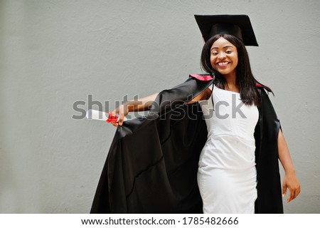 Young female african american student with diploma poses outdoors.
