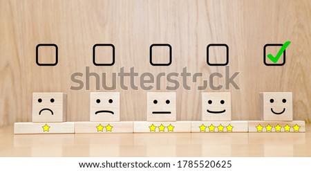 Customer service evaluation and satisfaction survey concepts. The selected checkbox happy face smile and five star symbol on wooden cube on table
