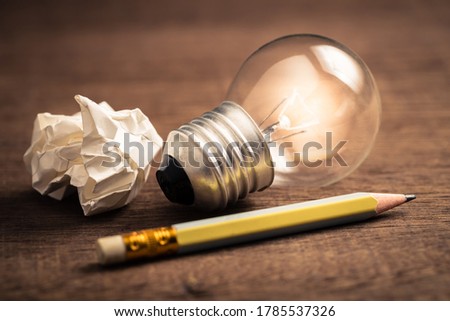 Pencil with glowing light bulb and crumpled paper on wood table, creative writing tips concept